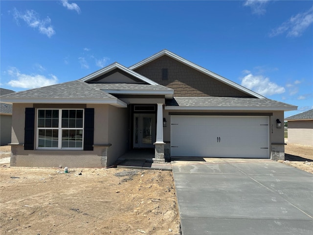 view of front of house with roof with shingles, an attached garage, stucco siding, and concrete driveway
