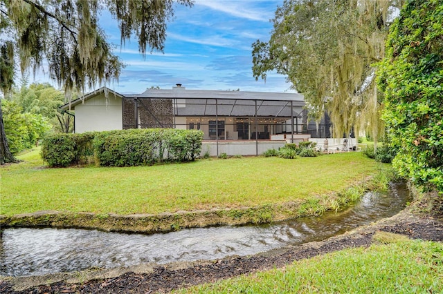 back of house with a yard, a water view, and a lanai