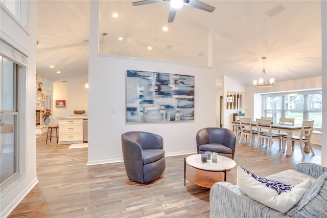 living room featuring vaulted ceiling, light hardwood / wood-style flooring, and ceiling fan with notable chandelier