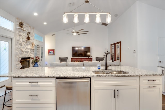 kitchen with stainless steel dishwasher, vaulted ceiling, sink, white cabinets, and a stone fireplace