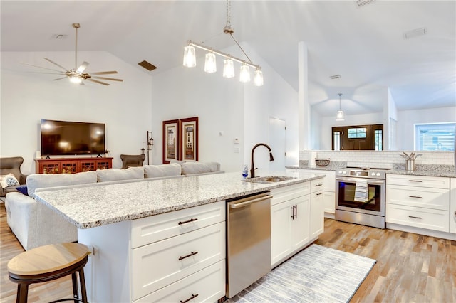 kitchen featuring sink, stainless steel appliances, vaulted ceiling, a kitchen bar, and a center island with sink