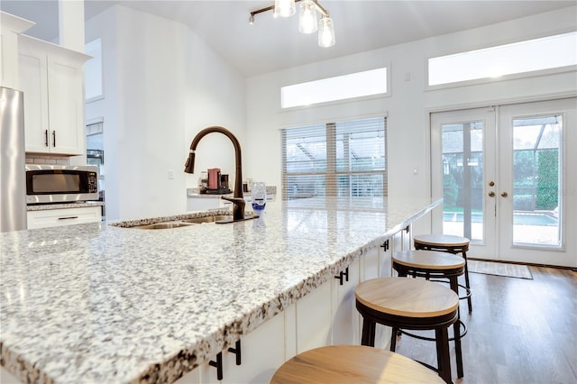 kitchen with french doors, light stone counters, stainless steel appliances, sink, and white cabinetry