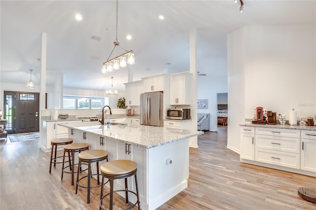 kitchen featuring white cabinets, stainless steel appliances, hanging light fixtures, and an island with sink