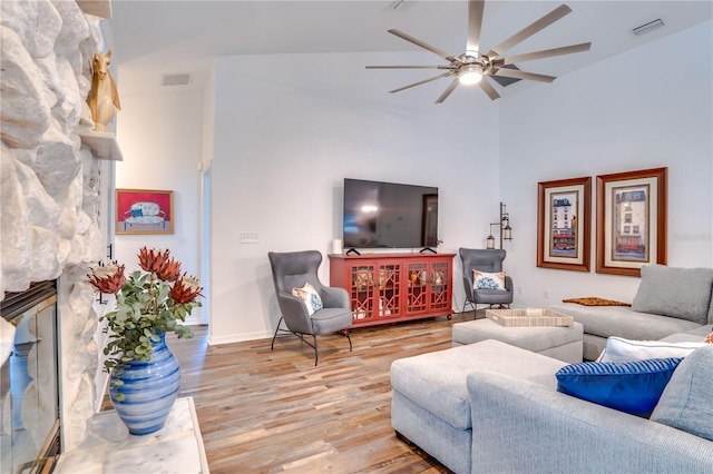 living room with a stone fireplace, ceiling fan, lofted ceiling, and light wood-type flooring