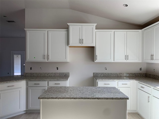 kitchen featuring white cabinetry, a center island, light stone countertops, and lofted ceiling