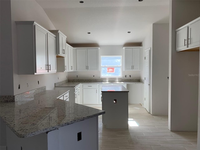 kitchen with kitchen peninsula, white cabinetry, a center island, and light stone countertops