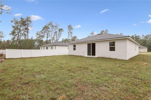 rear view of property featuring stucco siding, fence, and a lawn