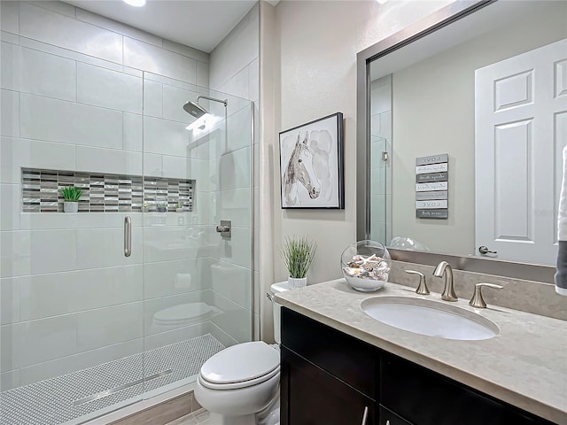 bathroom featuring a shower with door, vanity, and toilet