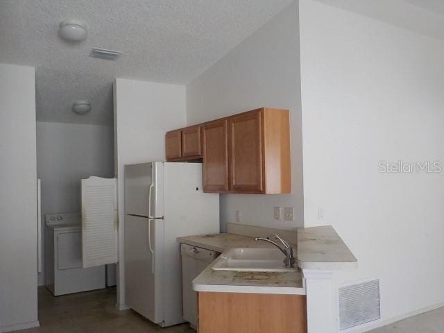 kitchen featuring a textured ceiling, white dishwasher, washer / clothes dryer, and sink