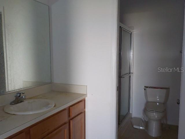 bathroom featuring a shower with door, vanity, and toilet