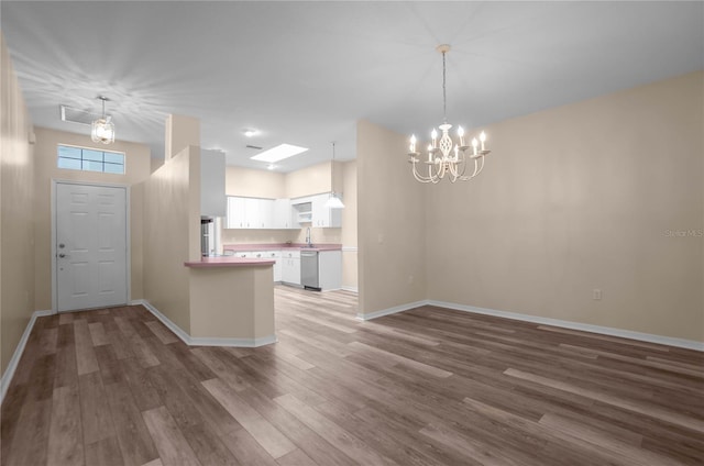 kitchen featuring dishwasher, dark wood-type flooring, a notable chandelier, kitchen peninsula, and white cabinets