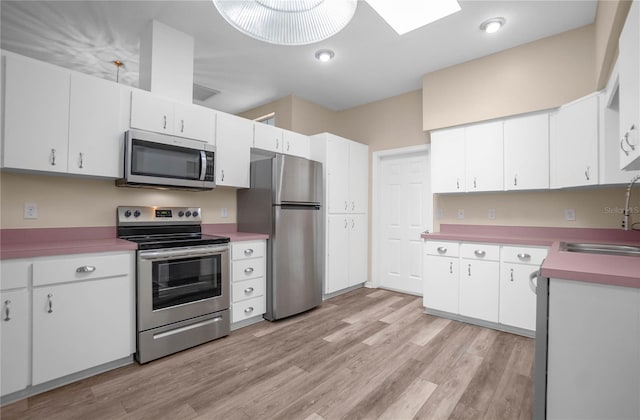 kitchen with a skylight, stainless steel appliances, sink, light hardwood / wood-style flooring, and white cabinets