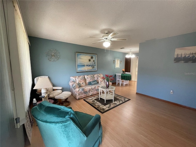 living room featuring ceiling fan with notable chandelier, wood-type flooring, and a textured ceiling