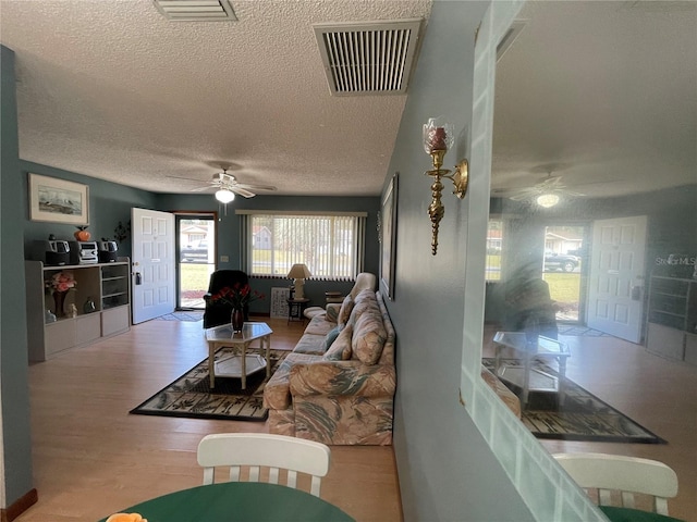 living room featuring ceiling fan, light hardwood / wood-style floors, and a textured ceiling