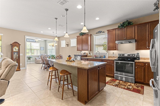 kitchen featuring light stone countertops, a center island, sink, stainless steel appliances, and pendant lighting