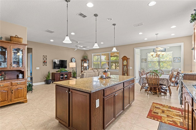 kitchen featuring a center island, ceiling fan with notable chandelier, hanging light fixtures, light stone countertops, and light tile patterned floors