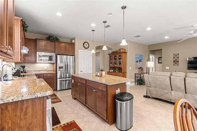 kitchen featuring a center island, hanging light fixtures, ceiling fan, light stone counters, and stainless steel appliances