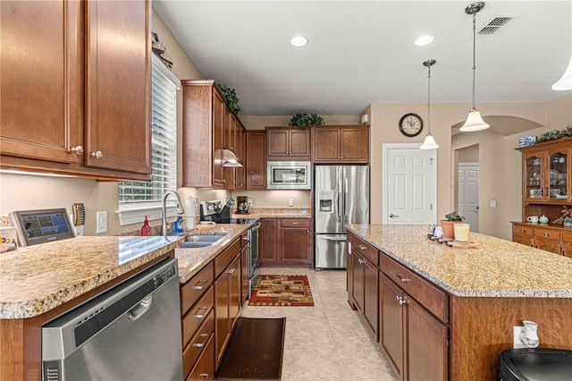 kitchen with light stone counters, stainless steel appliances, sink, decorative light fixtures, and a kitchen island