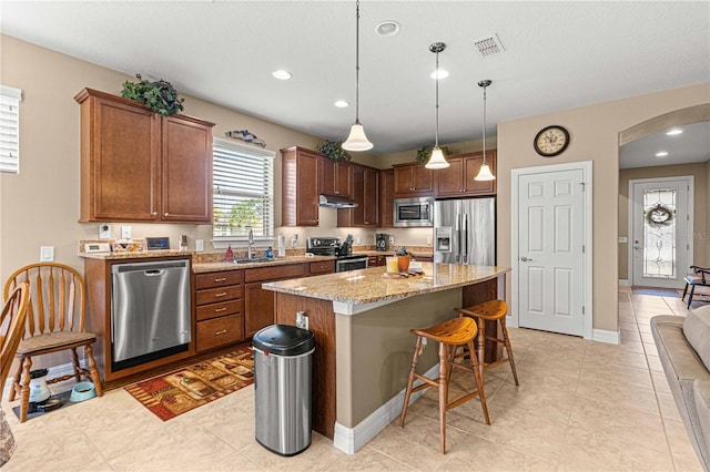 kitchen with pendant lighting, sink, a kitchen island, light stone counters, and stainless steel appliances