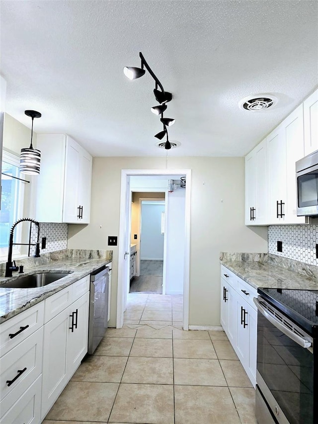 kitchen featuring backsplash, white cabinets, sink, appliances with stainless steel finishes, and decorative light fixtures