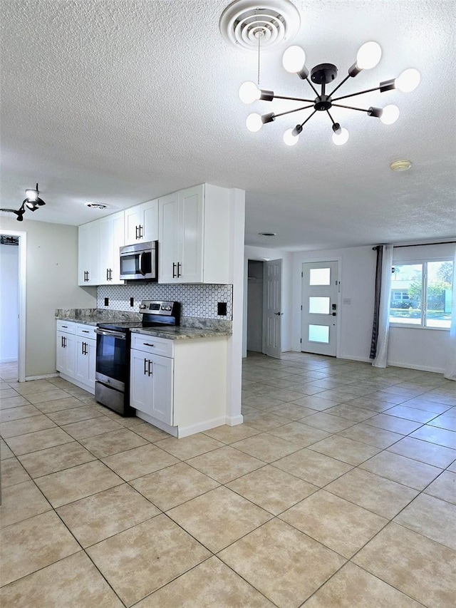 kitchen featuring white cabinets, appliances with stainless steel finishes, an inviting chandelier, and light stone counters