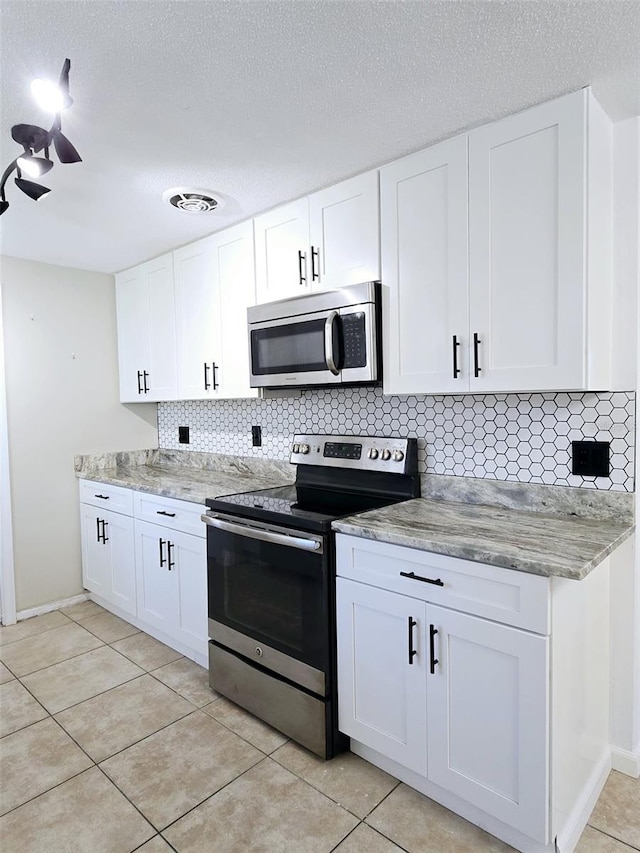 kitchen featuring decorative backsplash, a textured ceiling, stainless steel appliances, light tile patterned floors, and white cabinetry