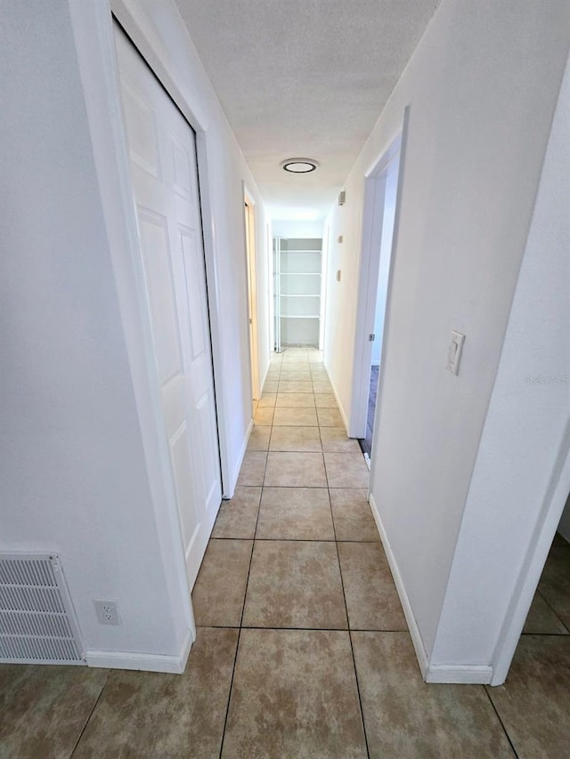 hall featuring built in shelves, light tile patterned floors, and a textured ceiling