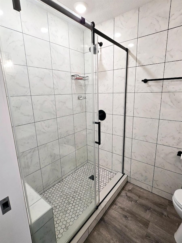 bathroom with hardwood / wood-style floors, a textured ceiling, toilet, and a shower with door