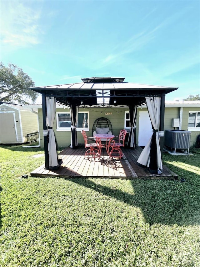 rear view of house featuring a storage shed, a wooden deck, a gazebo, central AC unit, and a lawn