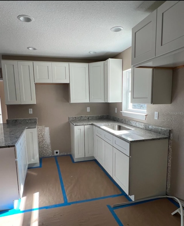 kitchen with a textured ceiling, white cabinetry, and sink