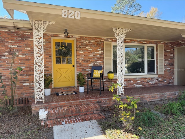 view of exterior entry with covered porch and brick siding