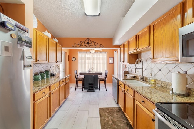 kitchen with sink, light stone counters, a textured ceiling, decorative backsplash, and appliances with stainless steel finishes