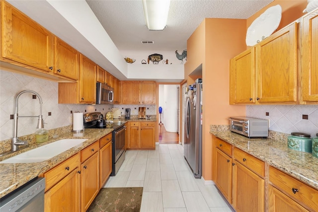 kitchen with sink, tasteful backsplash, light stone counters, light tile patterned floors, and appliances with stainless steel finishes