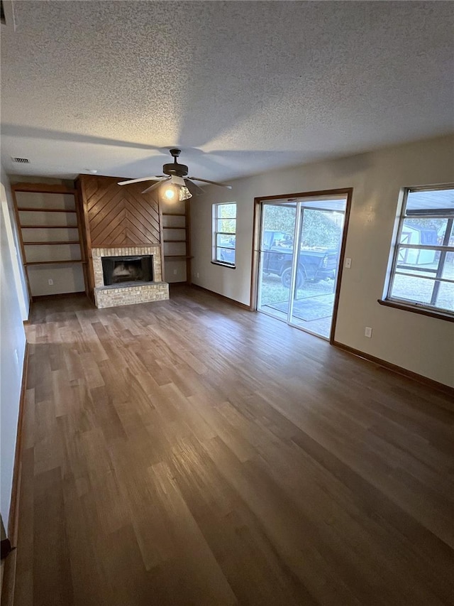 unfurnished living room with ceiling fan, wood-type flooring, a textured ceiling, and a brick fireplace