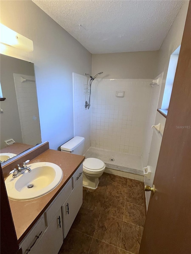 bathroom featuring vanity, toilet, a tile shower, and a textured ceiling