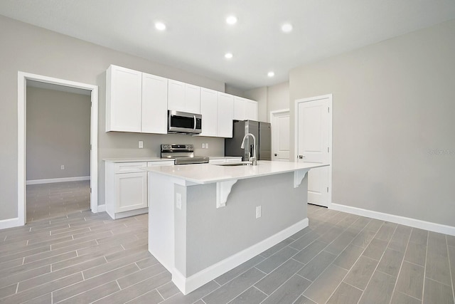 kitchen featuring white cabinetry, sink, stainless steel appliances, an island with sink, and a breakfast bar