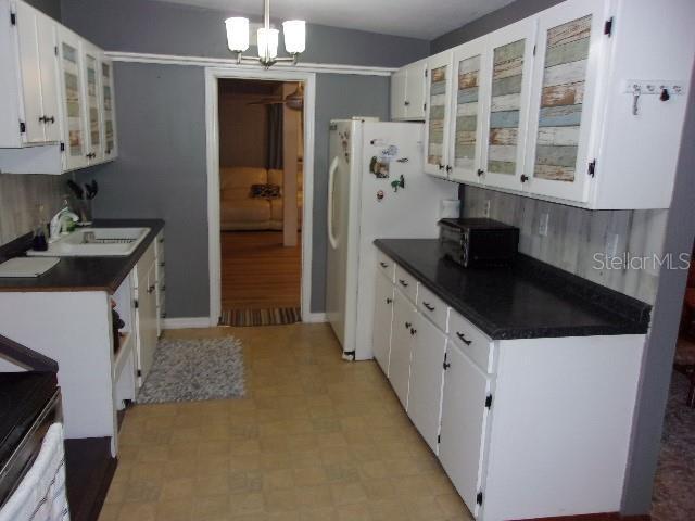 kitchen with white refrigerator, sink, decorative backsplash, a notable chandelier, and white cabinetry