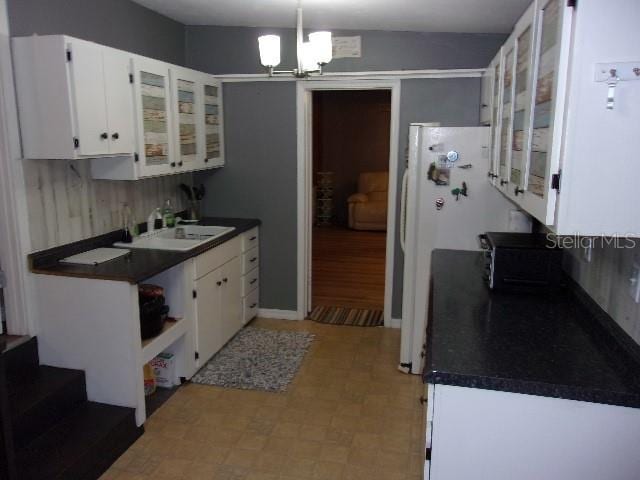 kitchen featuring white cabinets, white refrigerator, sink, and an inviting chandelier