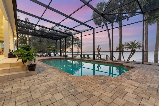 pool at dusk featuring a patio, a lanai, and a water view