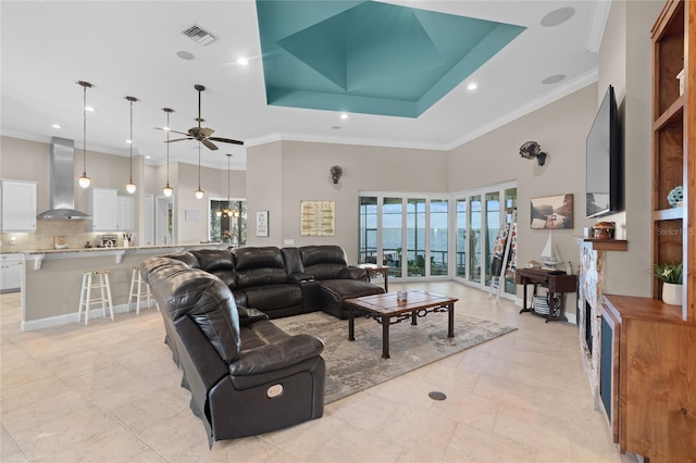 living room featuring a high ceiling, ceiling fan, a tray ceiling, and ornamental molding