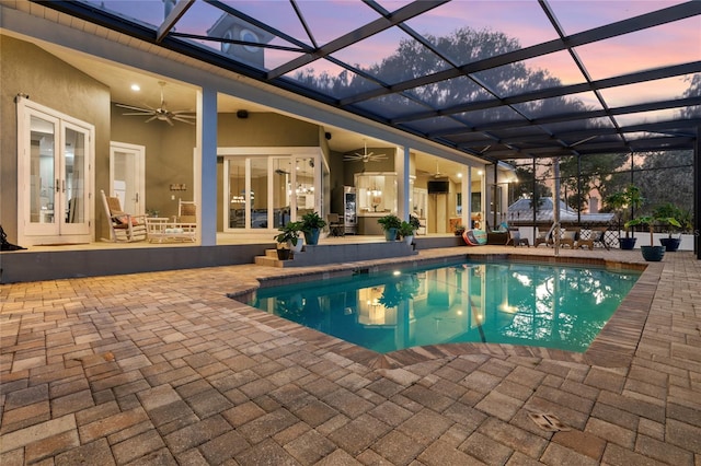 pool at dusk with ceiling fan, glass enclosure, and a patio