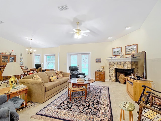 living room featuring a stone fireplace, french doors, light tile patterned floors, and ceiling fan with notable chandelier