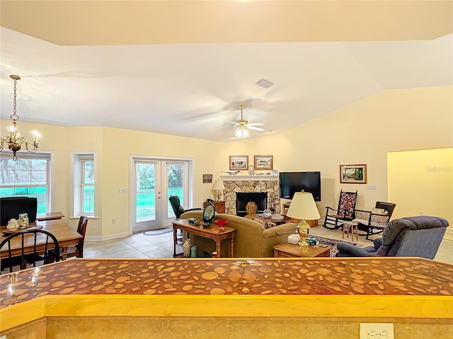 tiled living room featuring ceiling fan with notable chandelier, vaulted ceiling, a fireplace, and french doors