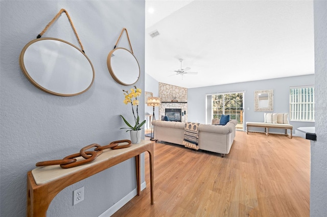 living room featuring lofted ceiling, ceiling fan, a stone fireplace, and light wood-type flooring