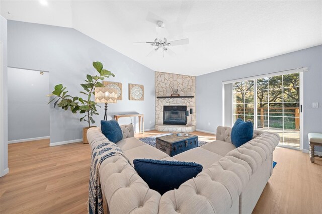 living room featuring a stone fireplace, ceiling fan, light hardwood / wood-style flooring, and vaulted ceiling