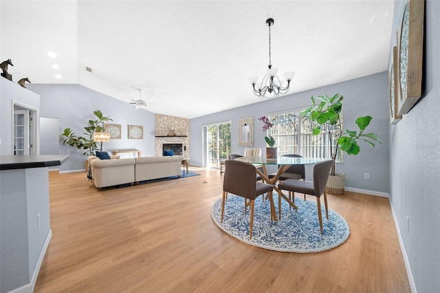 dining room featuring ceiling fan with notable chandelier, light hardwood / wood-style floors, a stone fireplace, and lofted ceiling