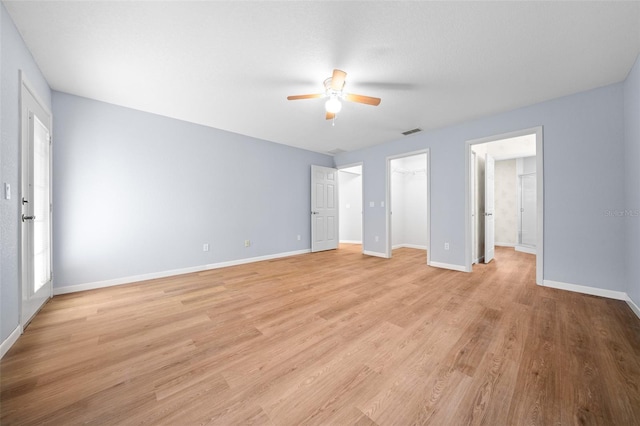 unfurnished bedroom featuring ceiling fan, ensuite bathroom, a walk in closet, a closet, and light wood-type flooring