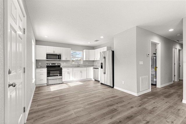 kitchen with light hardwood / wood-style flooring, white cabinets, stainless steel appliances, and a textured ceiling