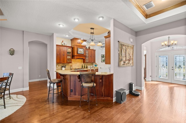 kitchen with pendant lighting, dark wood-type flooring, a kitchen breakfast bar, a raised ceiling, and kitchen peninsula