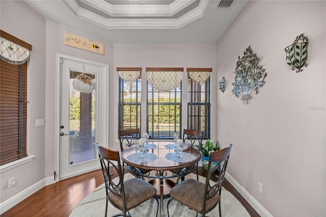 dining area with dark hardwood / wood-style flooring, a tray ceiling, and ornamental molding